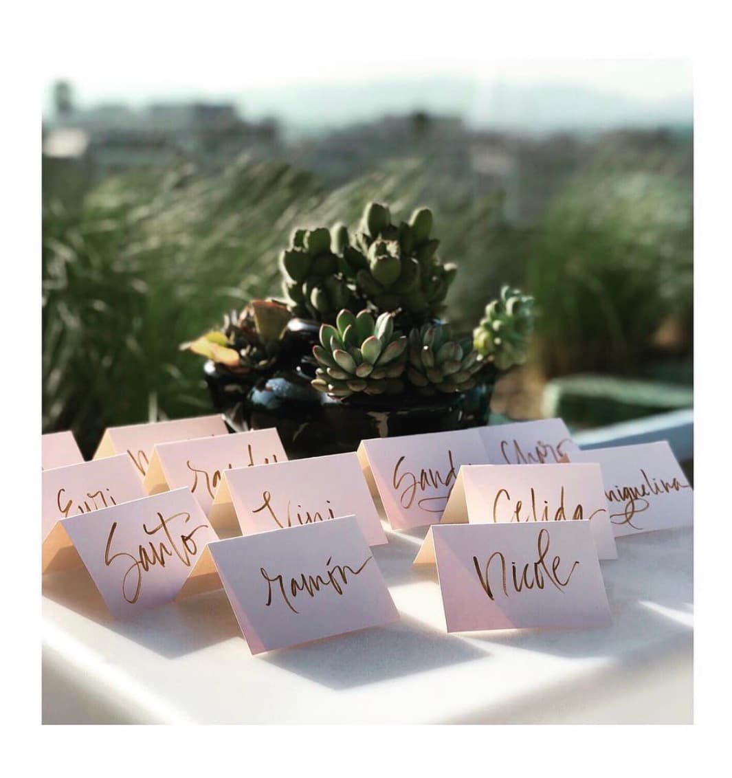 Hand-lettered place cards in gold ink beside succulents at a rooftop event